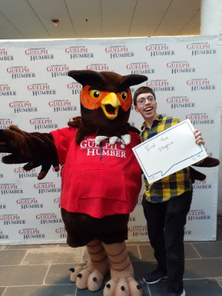 Student posing with Swoop mascot, holding sign with text: 'End the Stigma - Bell Lets Talk'